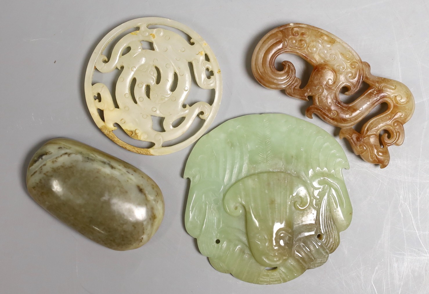 Four Chinese jade carvings, to include a face plaque, a dragon plaque, disc and a pebble carving, largest 6.5cm long, (4)